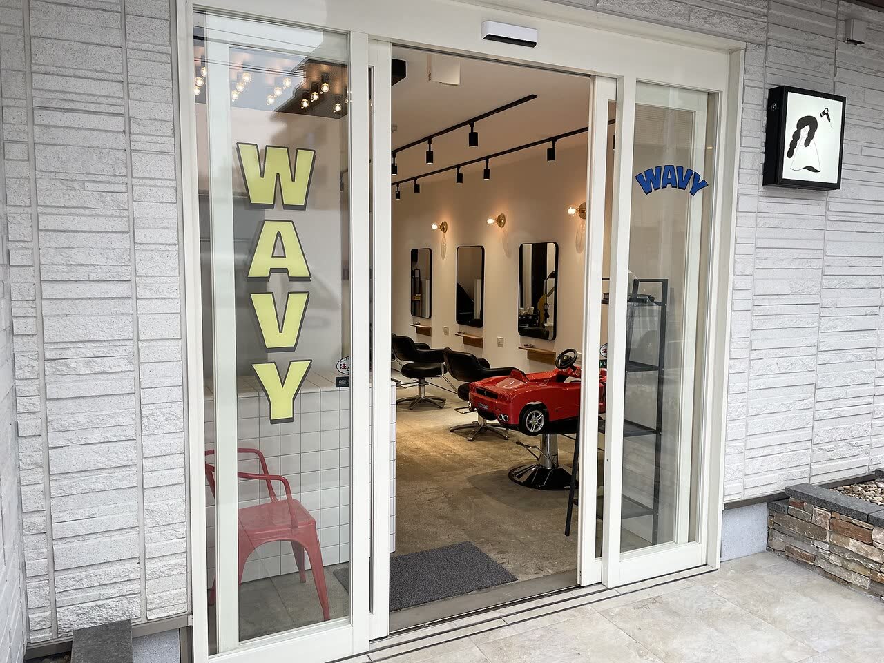 WAVYの入口。ガラス戸に黄色い文字でWAVY、奥に赤い車のキッズチェア